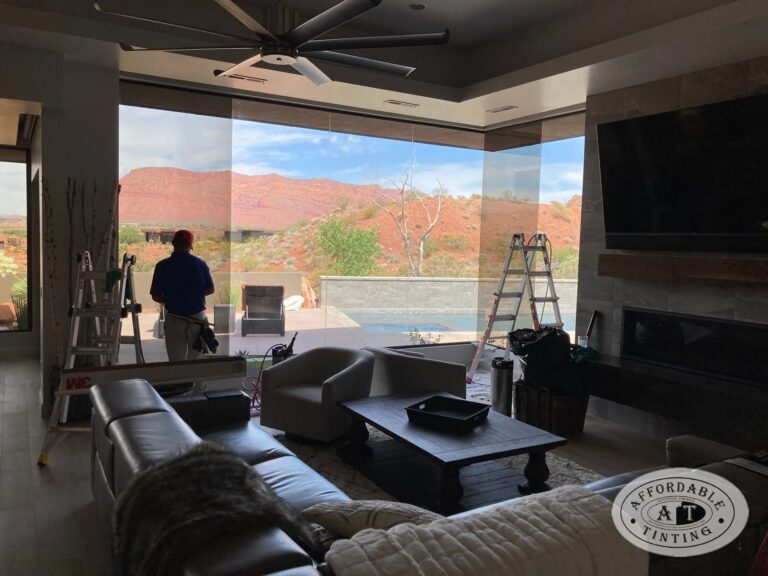 Affordable Tinting installer applying window film in a living room with a red rock view